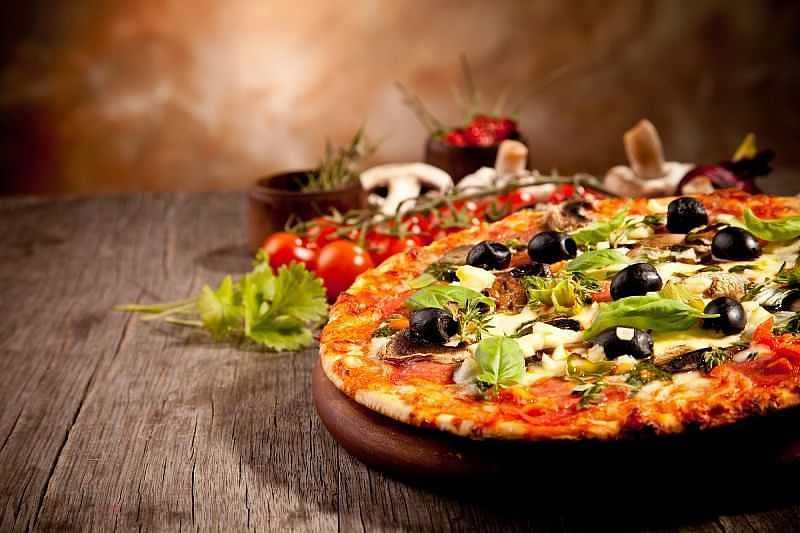 Vegetable pizza with olives, mushrooms, and greens on a rustic wooden table backdrop.